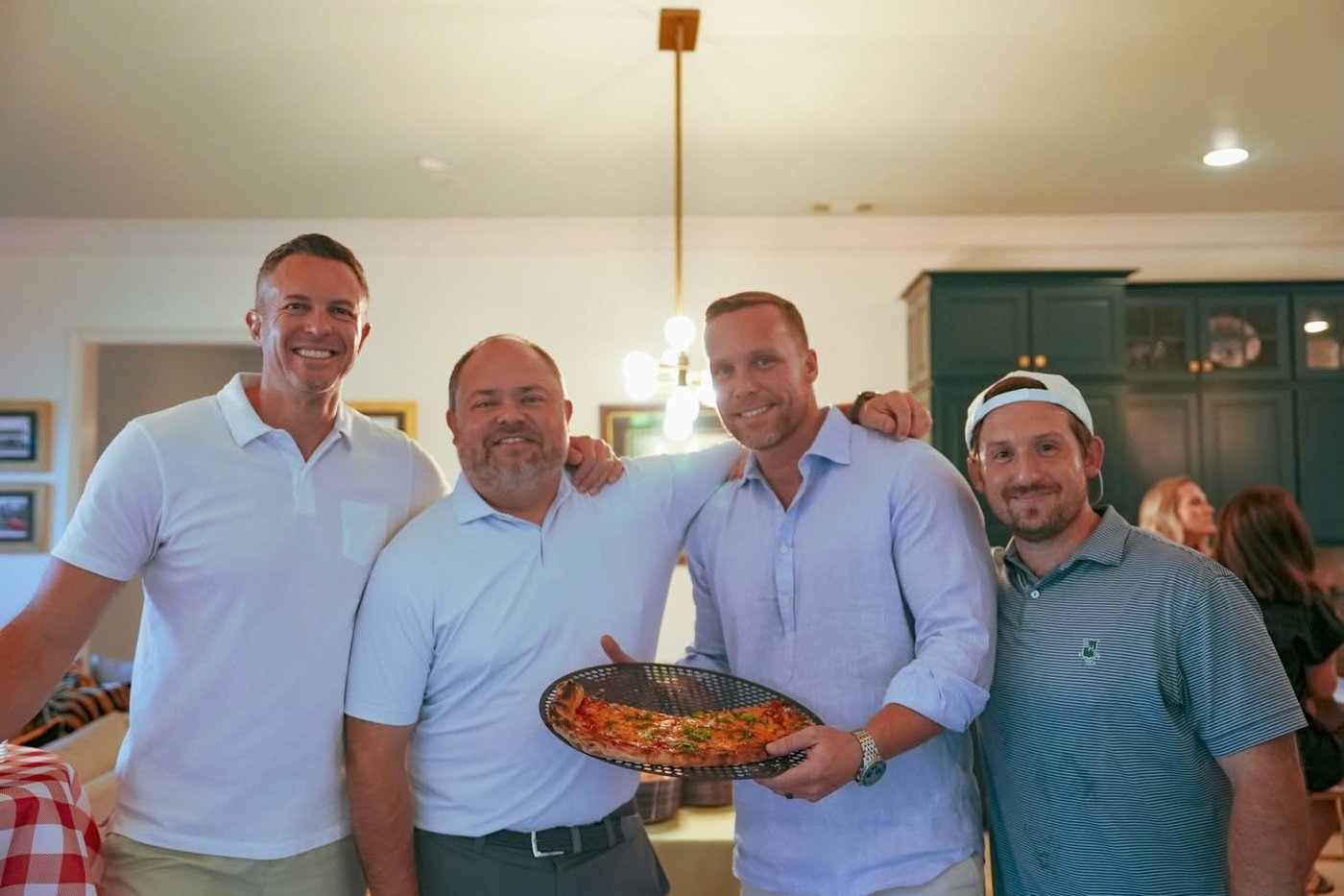 Four Veritas partners holding a fresh margherita pizza at the annual margs and margs party.