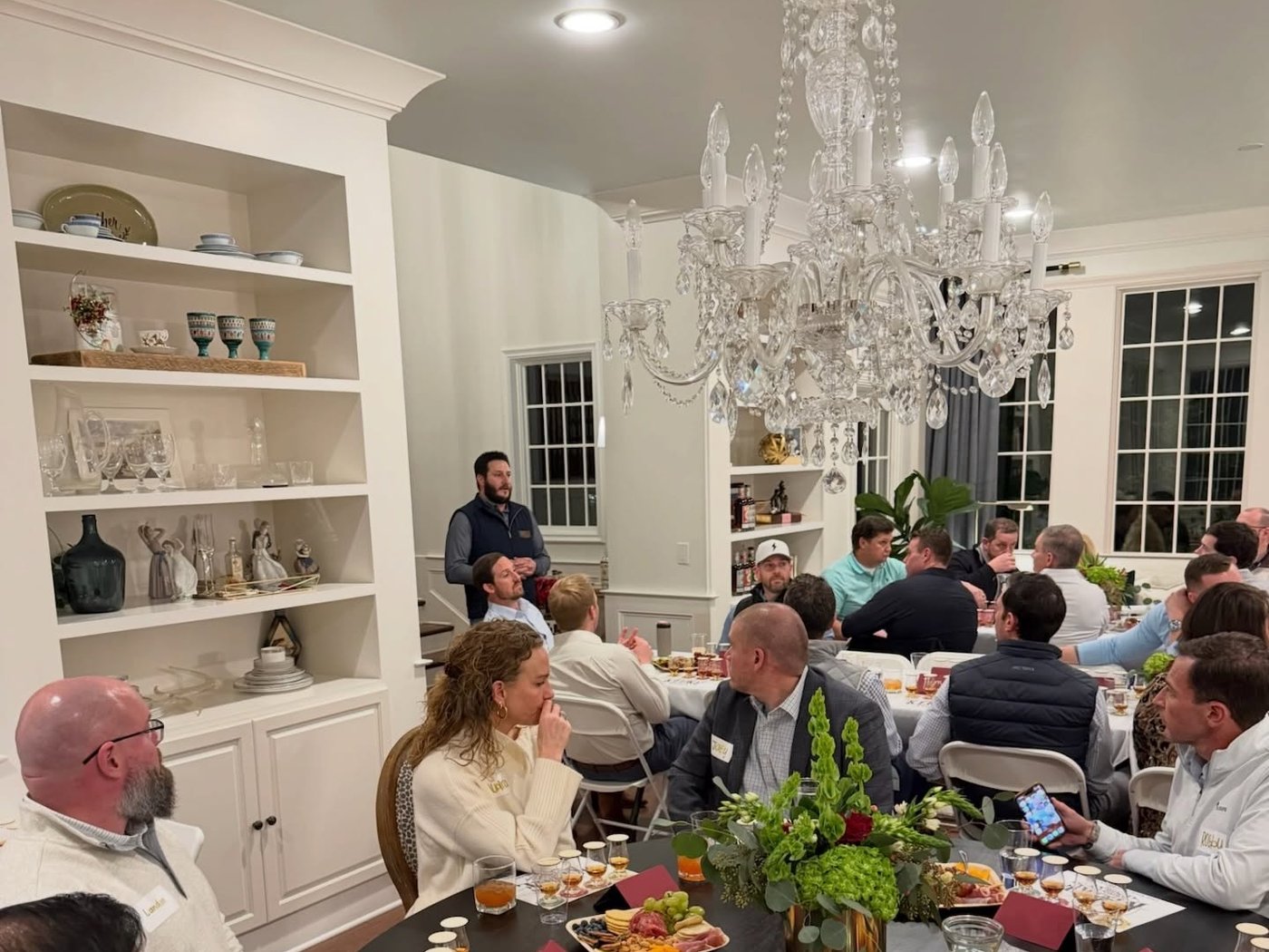 A full room of guests at a Veritas client event, seated at round tables under a chandelier.