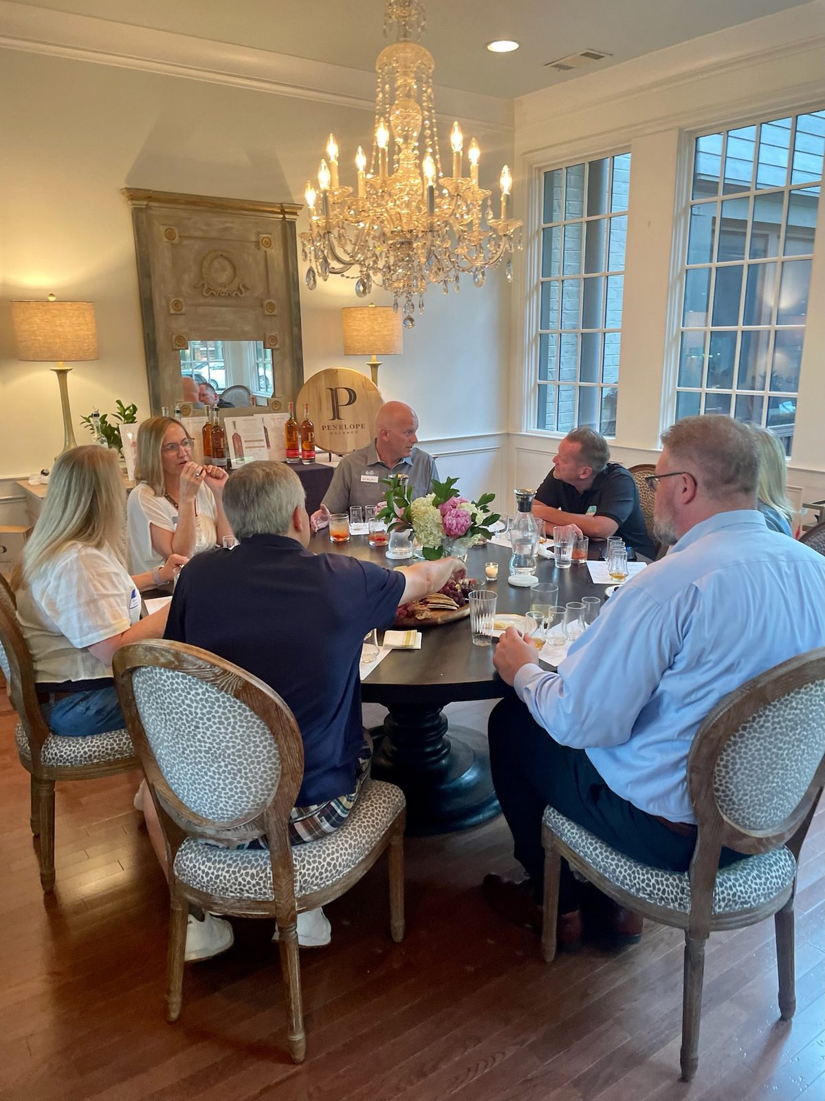 Guests in conversation around a round table under a chandelier at a Veritas event.